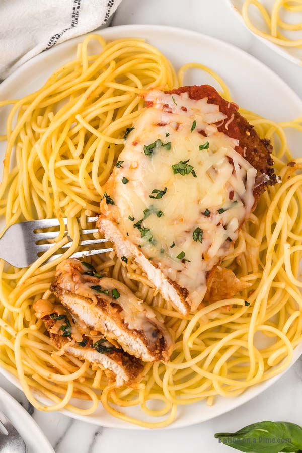 Chicken Parmesan on a white plate over pasta. 