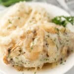 A plate with creamy mashed potatoes and Crockpot French Onion Chicken, topped with cooked onions and herbs, garnished with parsley.