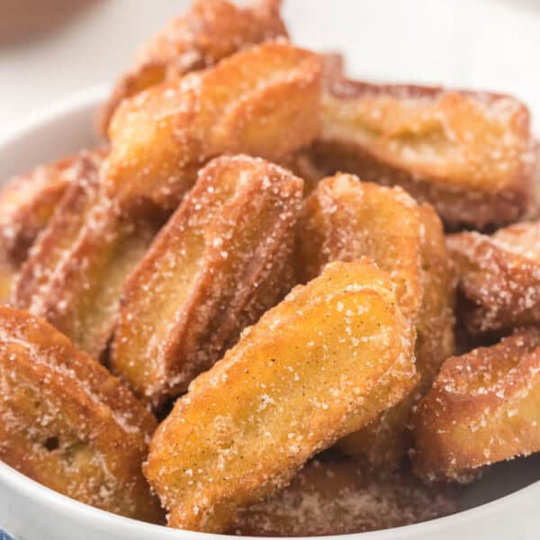 A bowl filled with golden-brown churro bites, crafted from a Copycat Disney Churro Recipe, coated in cinnamon sugar. These crispy delights are stacked on top of each other, bringing a touch of magic to your snack time.