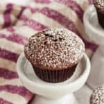 A mini brownie bite topped with powdered sugar on a small white pedestal.