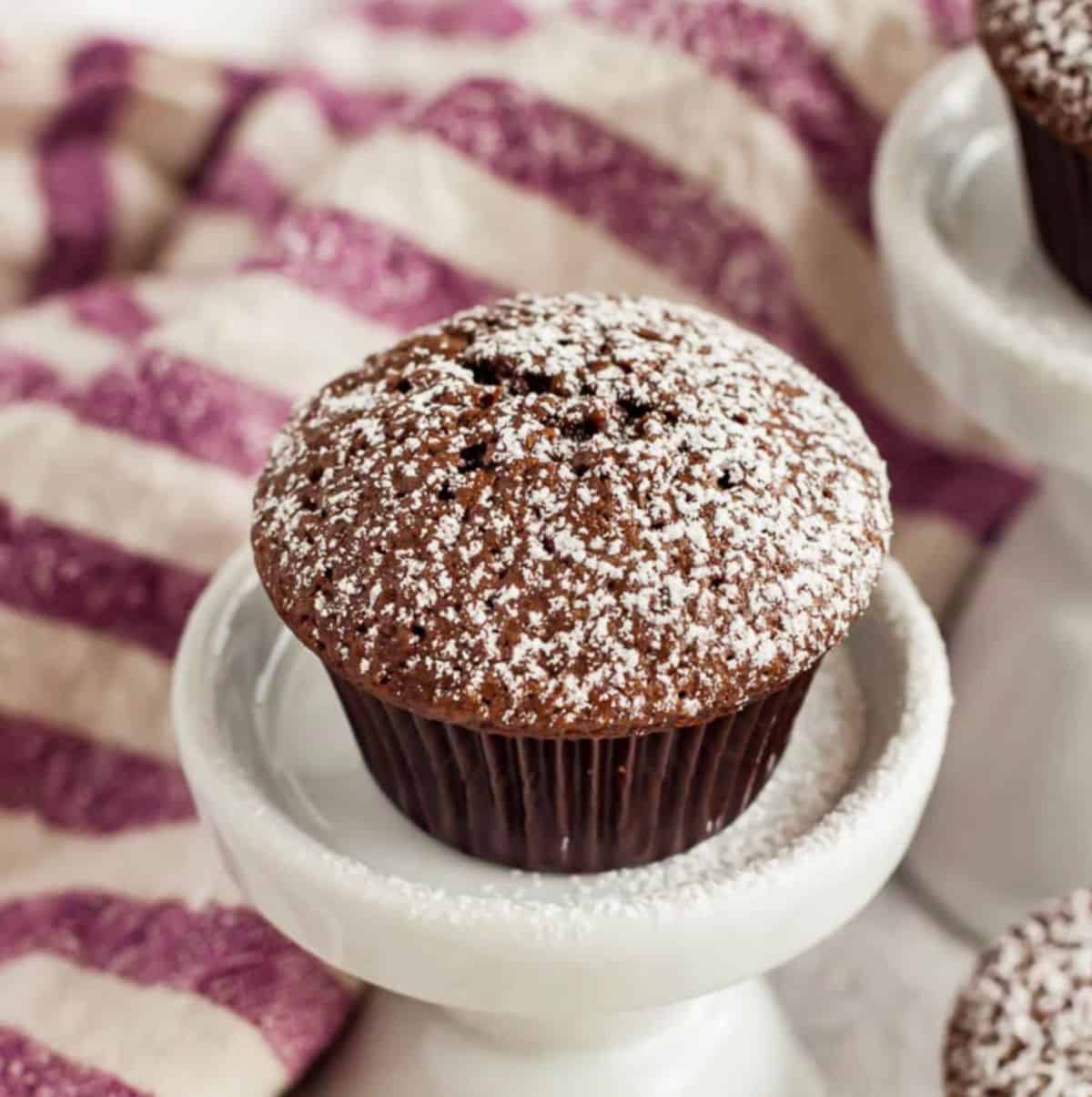 A mini brownie bite topped with powdered sugar on a small white pedestal.