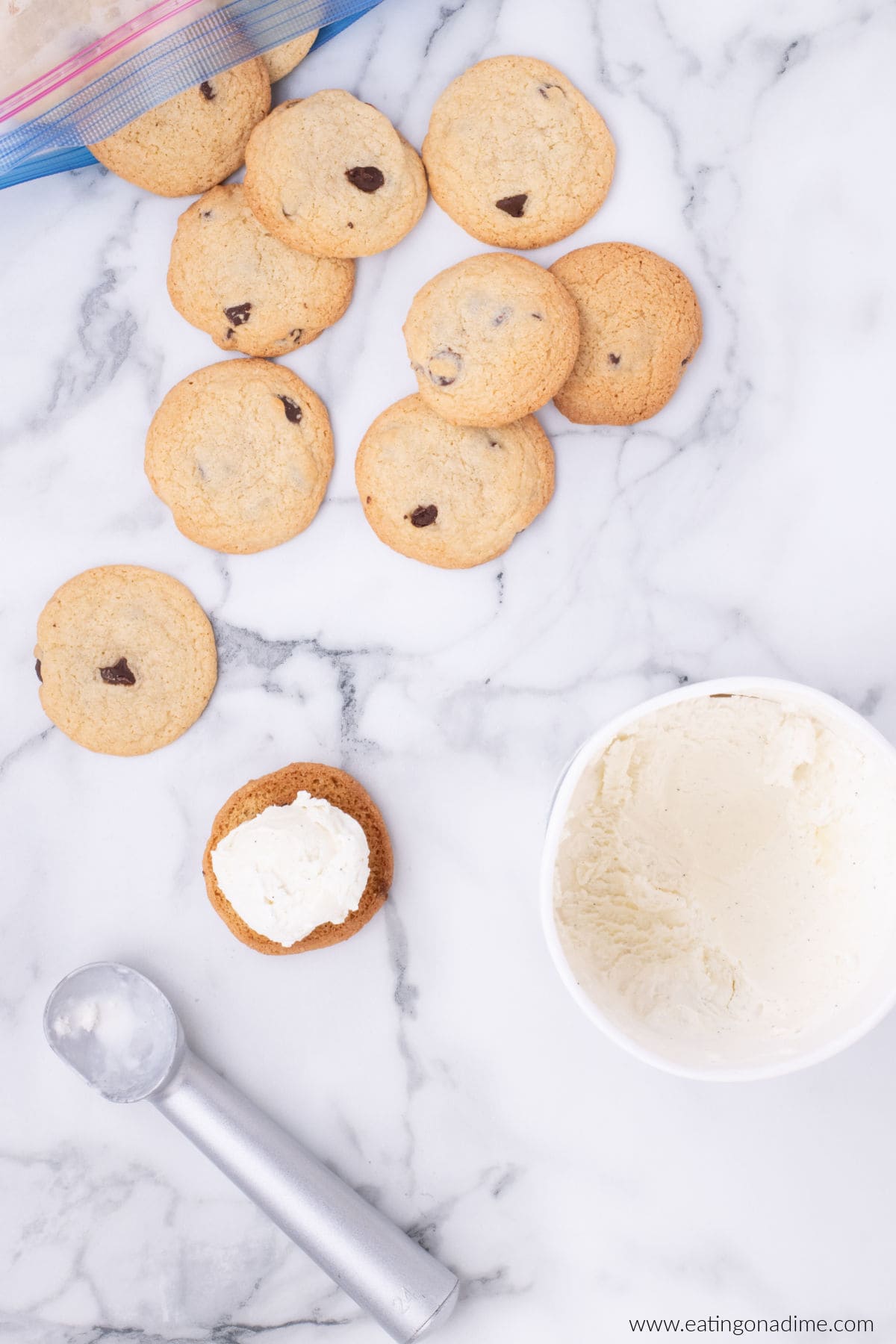 Scooping ice cream on the bottoms of baked chocolate chip cookies.