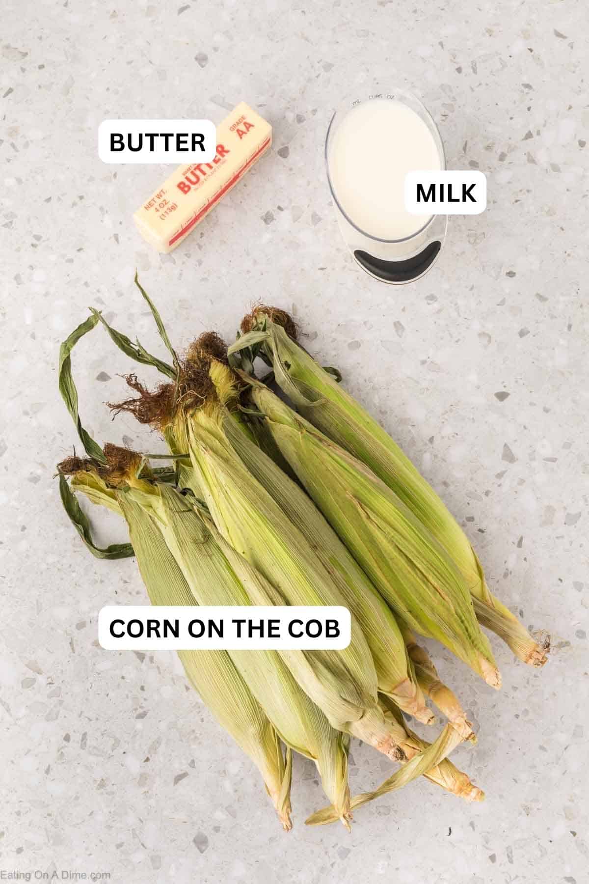 Ingredients needed to make this recipe which includes stick of butter, cut of milk and corn on the cob covered with husks.