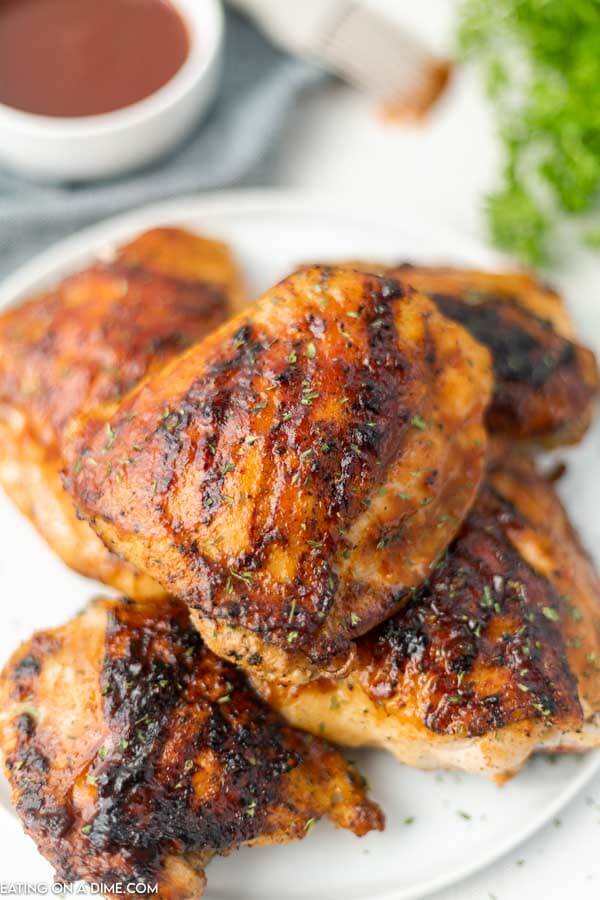 Grilled BBQ chicken thighs stacked on a plate. 