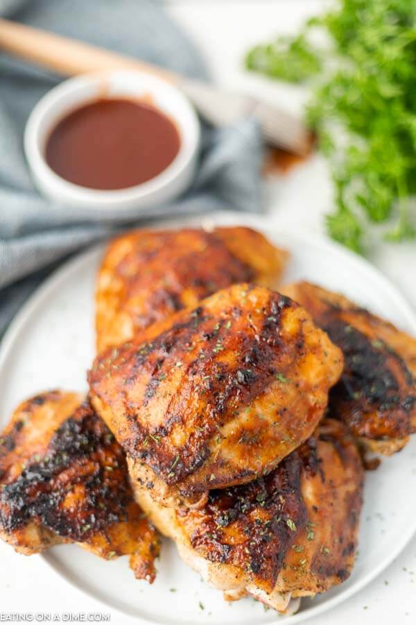 Grilled BBQ chicken thighs stacked on a plate. 