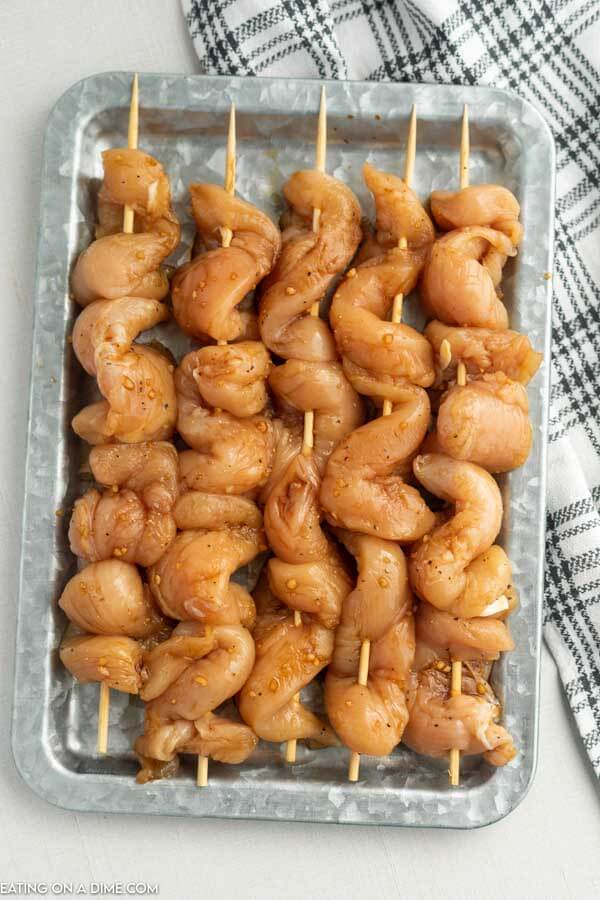 Chicken on a stick uncooked in a baking dish. 