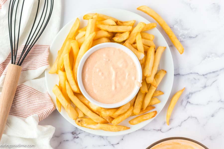 Close up image of big mac sauce in a white bowl with a side of french fries. with a whisk. 