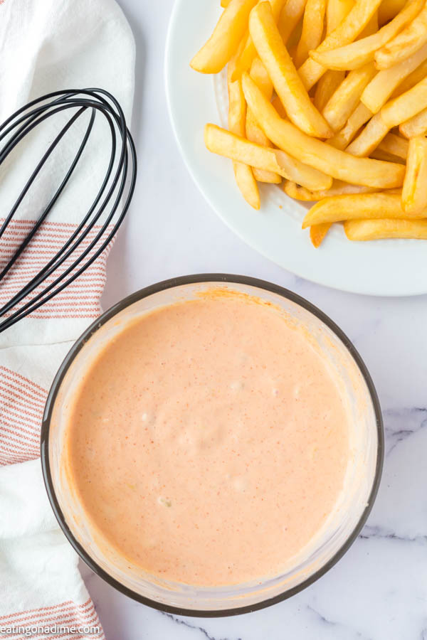 Close up image of big mac sauce in a clear bowl with a side of french fries. 
