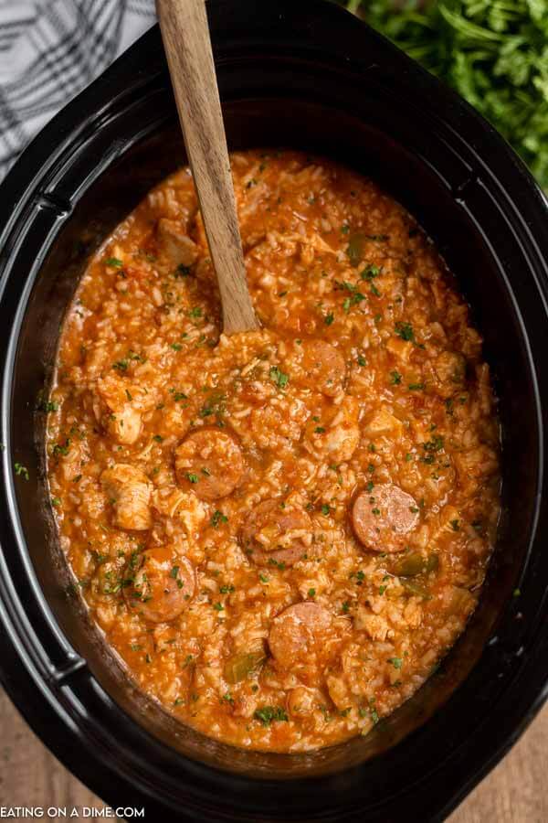 Close up image of chicken jambalaya in the crock pot with a wooden spoon. 