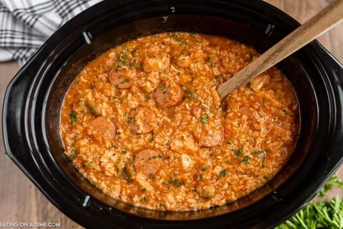 Close up image of chicken jambalaya in the crock pot with a wooden spoon. 