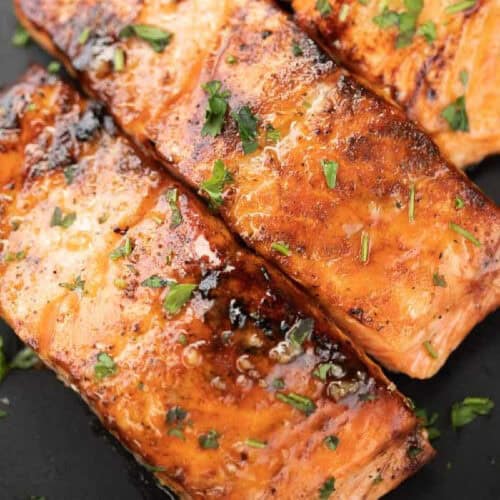 Planks of salmon on a black platter topped with fresh parsely.