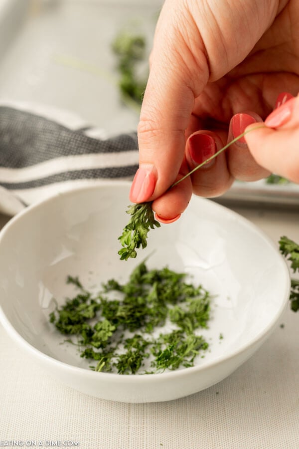 close up image of parsley being removed form the stems and put in a white bowl. 