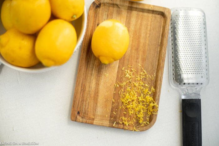 Close up image of lemons in a bowl with a cutting board and a zester. Also a zest on the side.