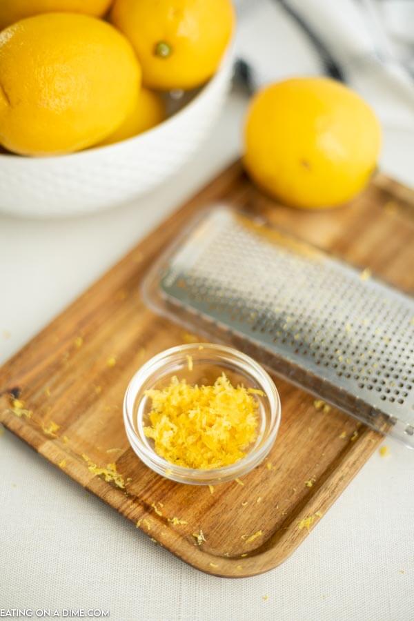 Close up image of lemons in a bowl with a cutting board and a zester. Also a zest. 