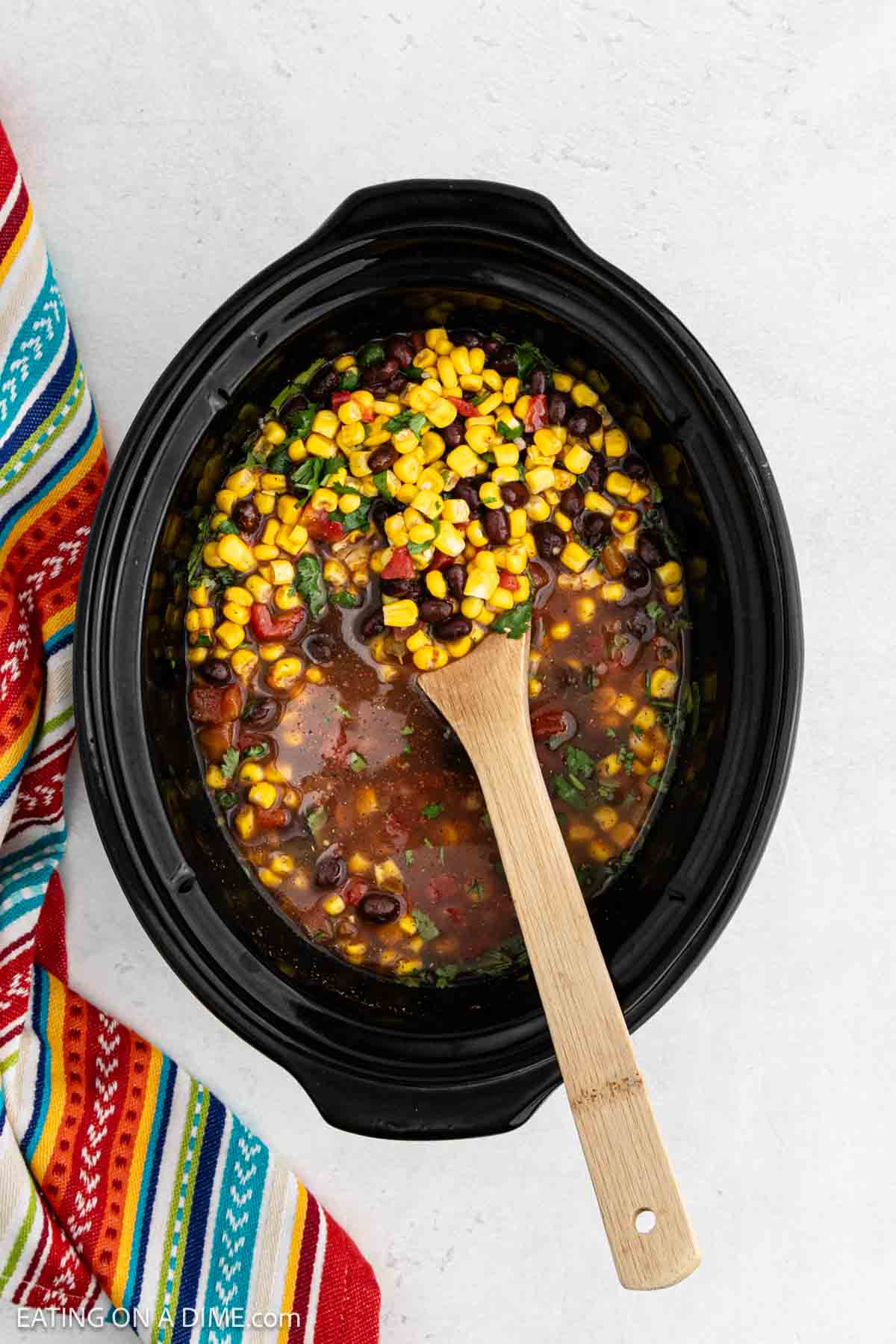 Combining the corn, diced tomatoes, cilantro, chicken broth in the slow cooker with the wooden spoon