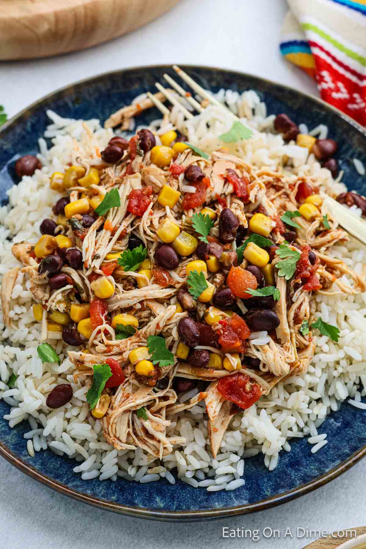 Shredded cooked chicken mixed with corn, black beans and diced tomatoes topped with fresh cilantro served over white rice on a plate