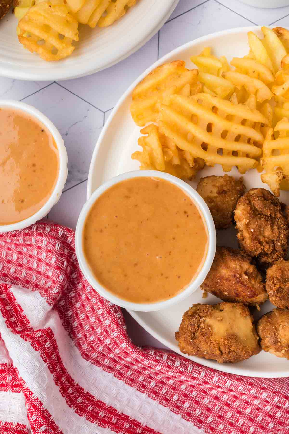 A small bowl of Chick Fil A Honey Roasted BBQ Sauce on a plate with fried chicken nuggets and french fries