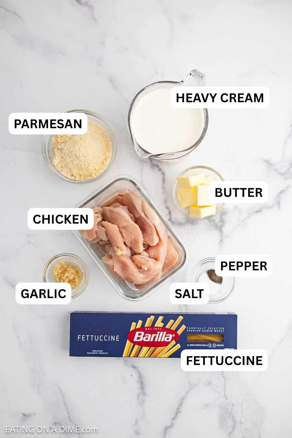 Ingredients needed to make this recipe which includes raw chicken strips, Barilla fettuccine, grated parmesan, minced garlic, butter cubes, milk in a measuring cup, and a small bowl of black pepper.