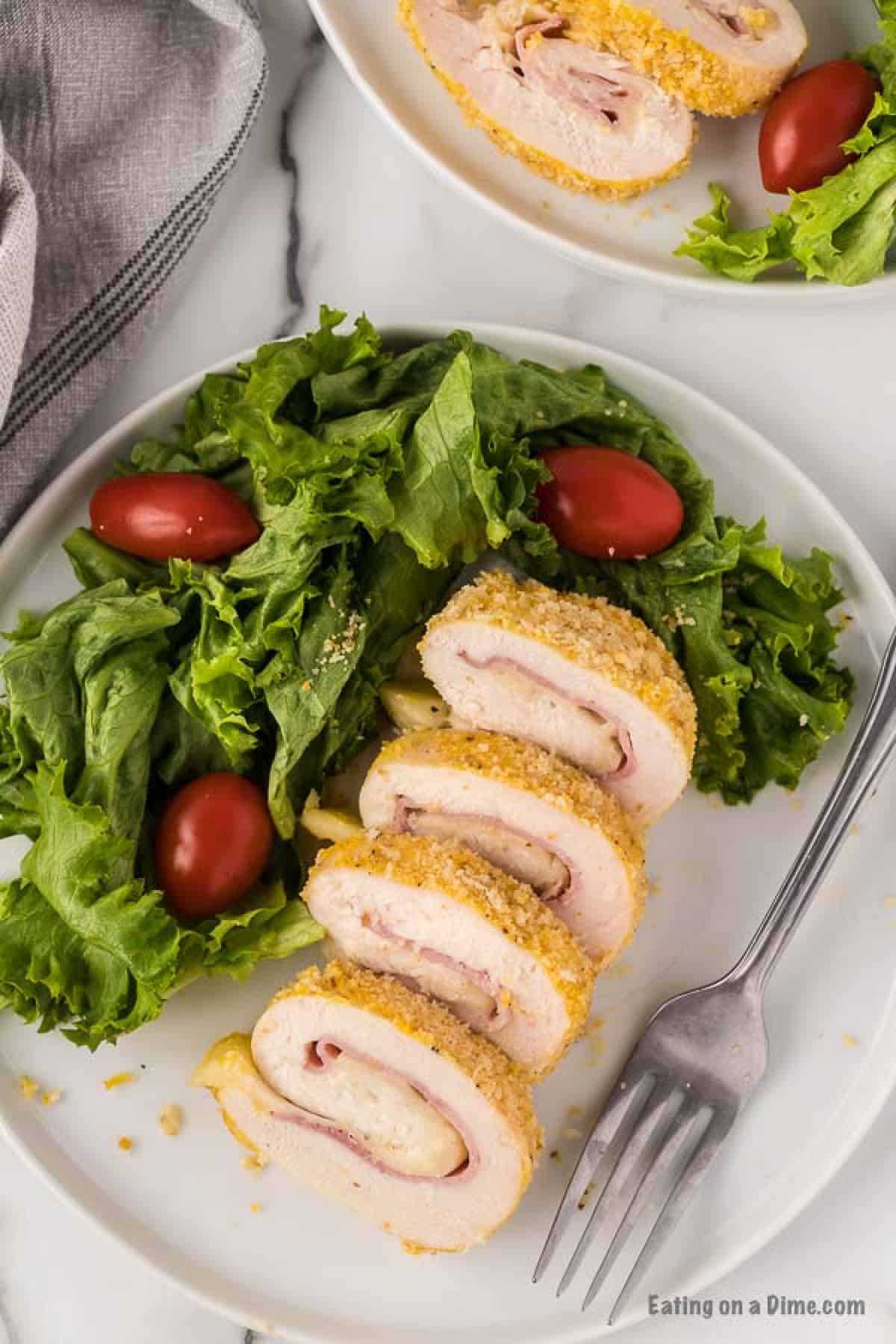 Close up image of chicken cordon bleu on a white plate with a side salad.