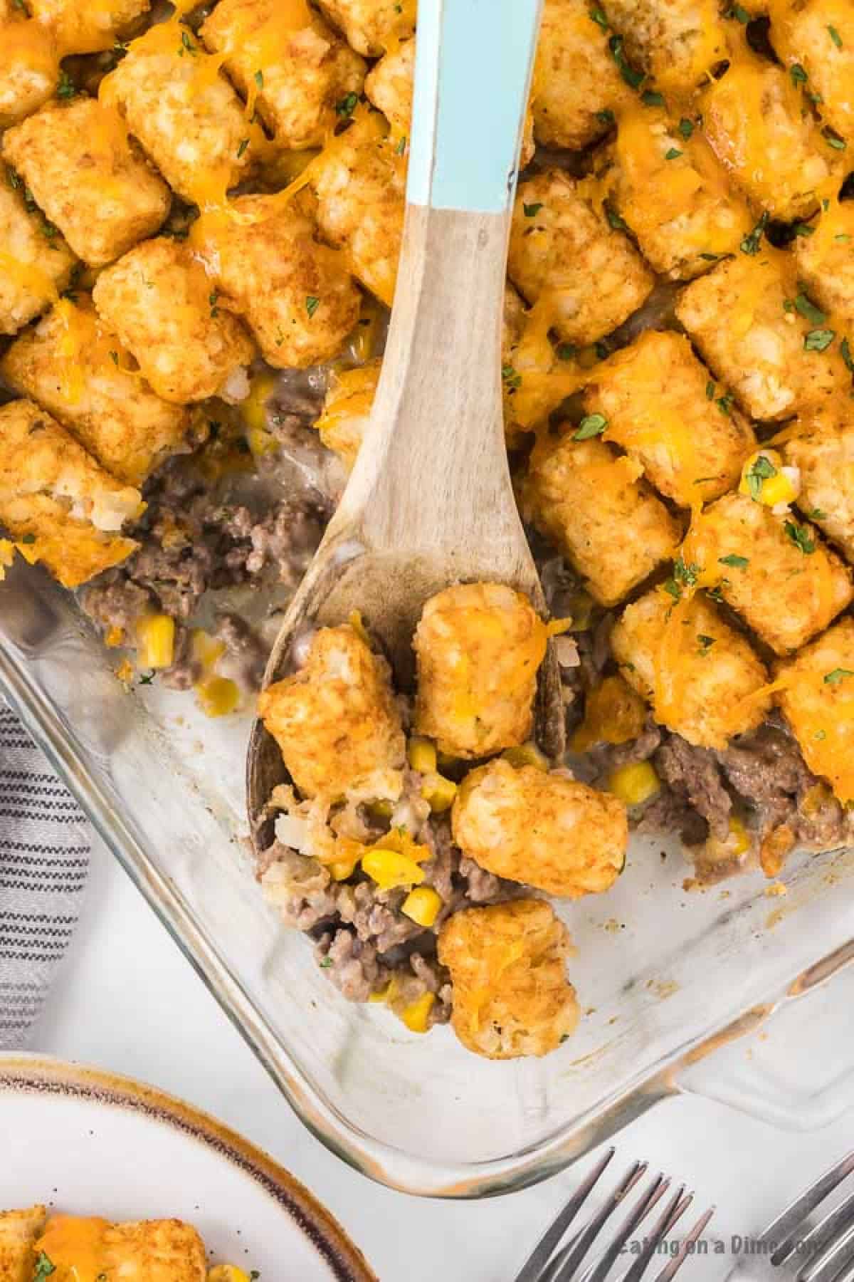 Close up image of cowboy casserole in a baking dish with a serving on a wooden spoon. 