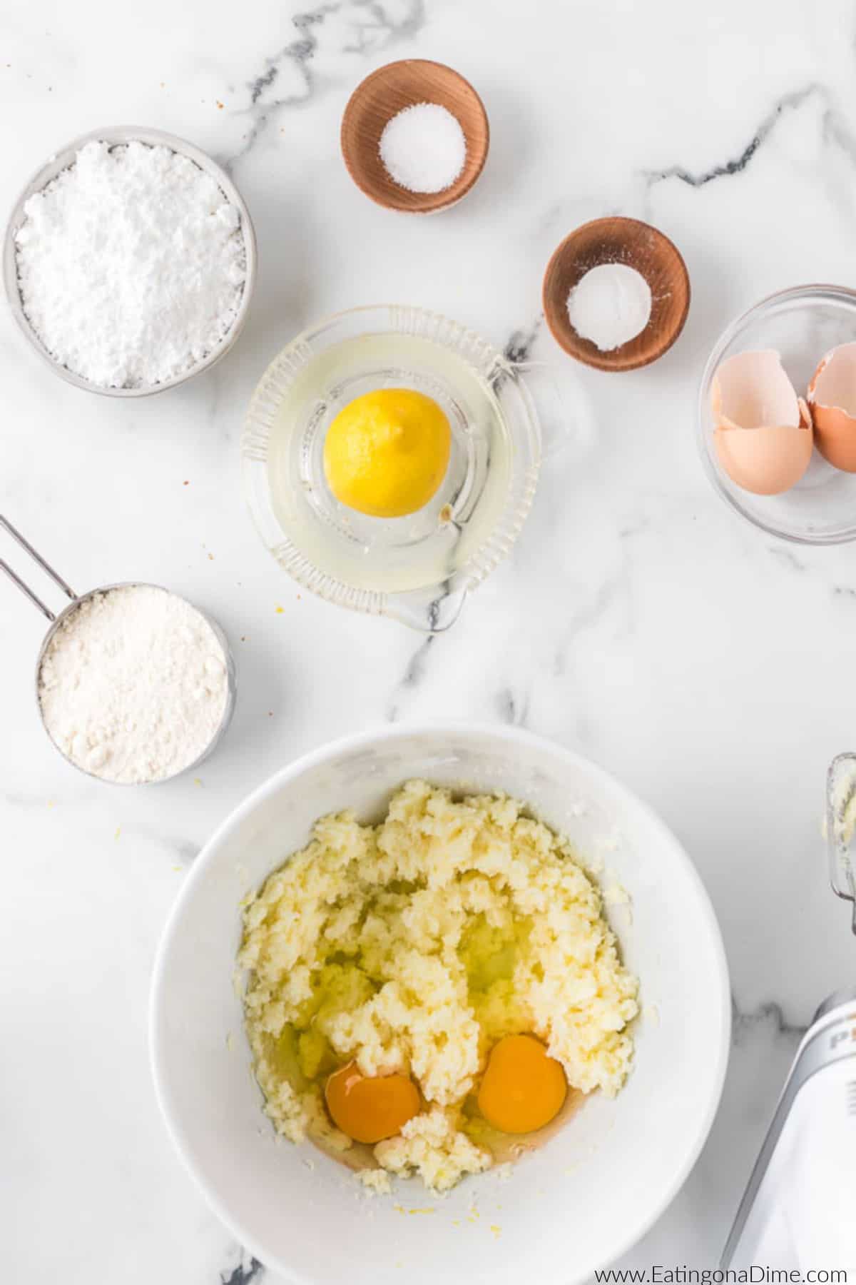 Eggs added to the lemon mixture in a bowl with small bowls of flour, powdered sugar, baking powder, and salt nearby.