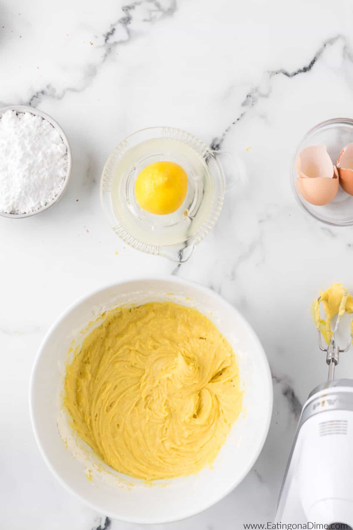 Batter in a bowl with a small bowl of fresh lemon and powdered sugar nearby.