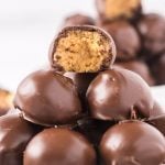 A close-up of several round Chocolate Peanut Butter Balls with Rice Krispies stacked on top of each other, with one truffle on top showing a bite revealing a creamy, light brown peanut butter filling inside.