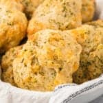 Close-up of golden-brown, fluffy Cheddar Bay Biscuits sprinkled with herbs, piled on a white cloth. The textured surface of these Red Lobster favorites is arranged in a bowl, highlighting their savory appearance.