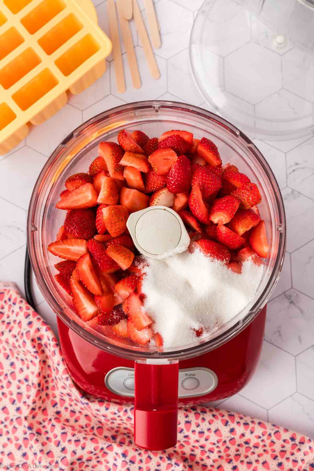 Chopped strawberries, sugar and honey in a food processor with a popsicle mold on the side