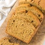 Sliced loaf of homemade zucchini bread on a wooden cutting board, with a few slices spread out in front. A white cloth is visible in the background, showcasing the results of this delicious zucchini bread recipe.