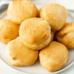 A plate with a stack of golden-brown, freshly baked biscuits made from canned dough in an air fryer. The biscuits are round with a slightly flaky texture and have a warm, inviting appearance. The plate is set on a light-colored surface.