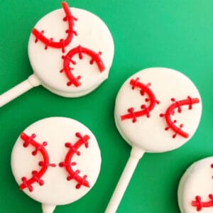 Four white baseball Oreo pops decorated with red stitching to resemble baseballs, arranged on a bright green background.