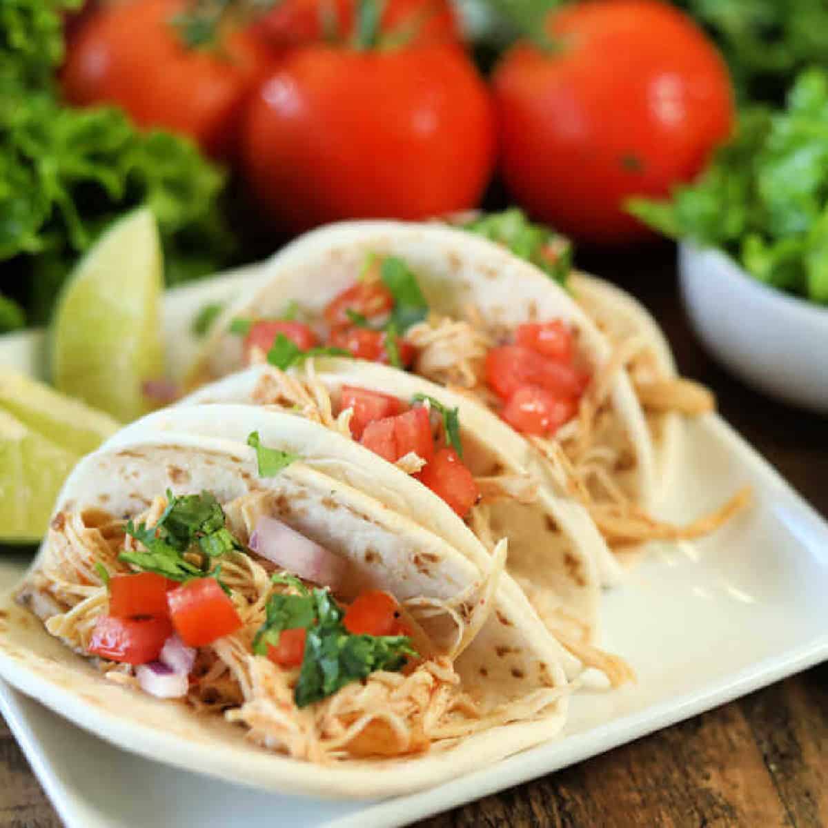 Close up image of chicken ranch tacos on a white platter with a side of red onion and tomatoes and lettuce.