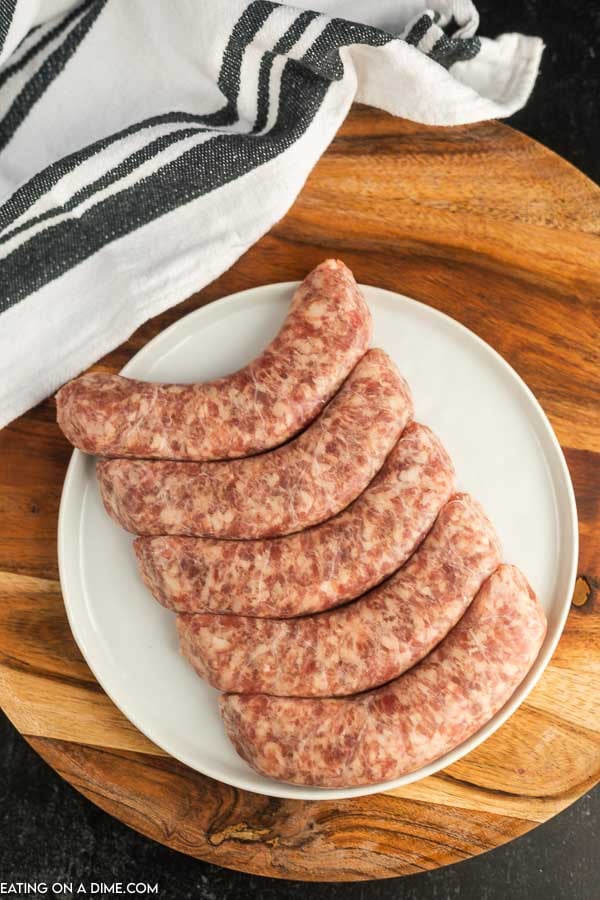 Uncooked brats on a white plate. 