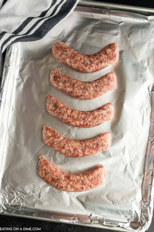 Uncooked brats on a foil lined baking sheet. 