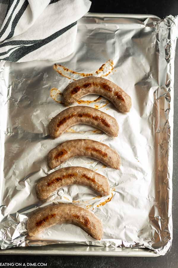 Close up image of cooked brats on a foil lined baking sheet. 