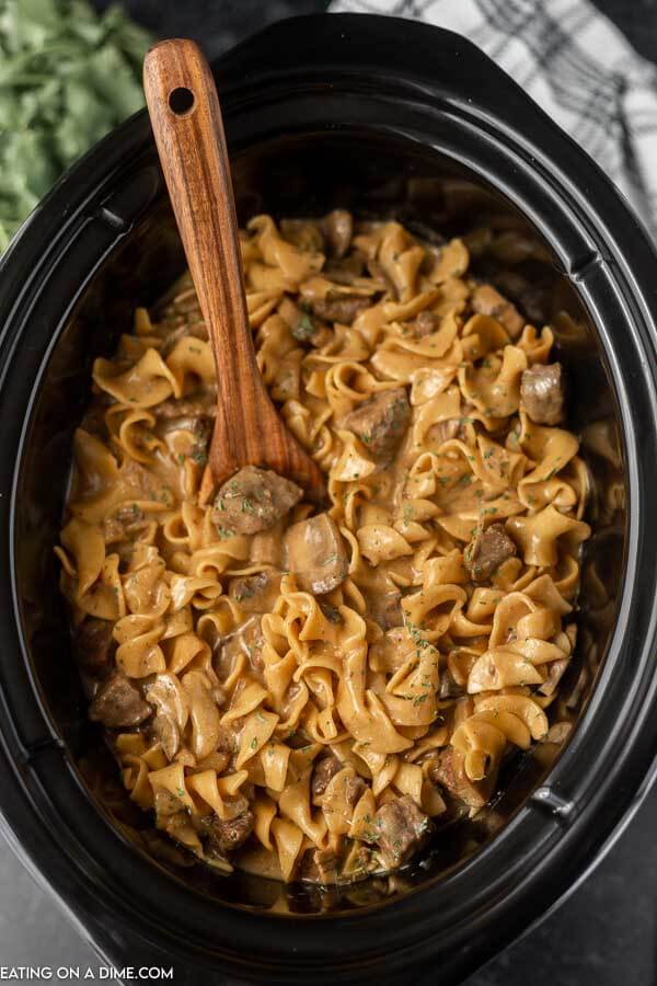 Close up image of beef stroganoff in the crock pot with a wooden spoon.