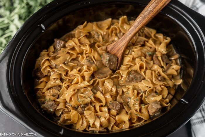 Close up image of beef stroganoff in the crock pot with a brown wooden spoon. 
