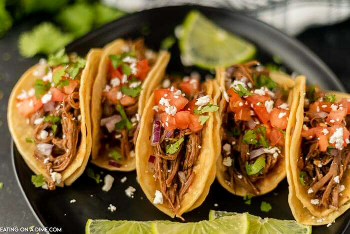 Close up image of 5 street tacos filled with carna asada on a plate. 