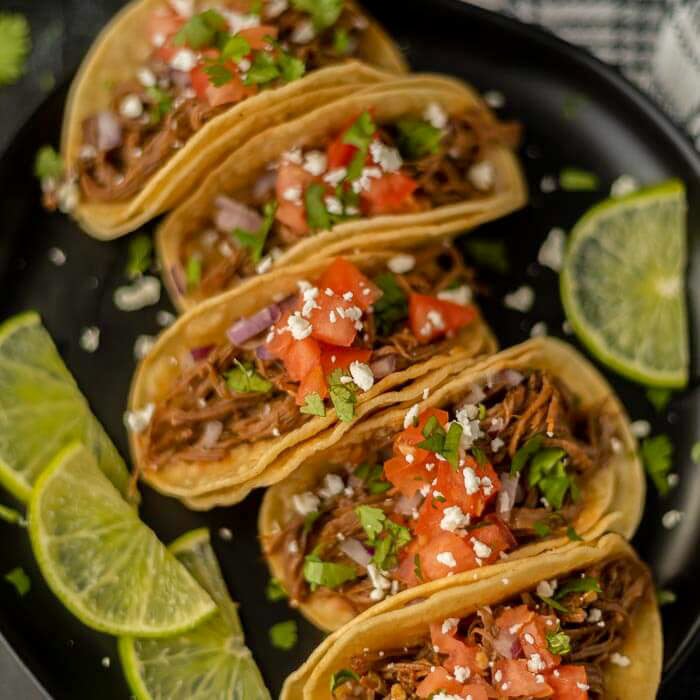 Close up image of street tacos on a plate with a side of limes. 