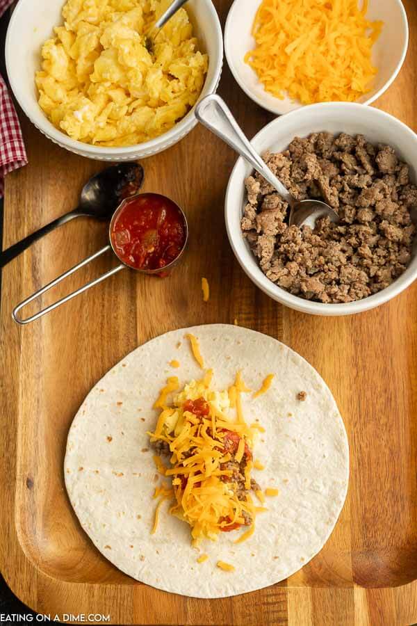 Layering eggs, sausage, and cheese on a flour tortilla