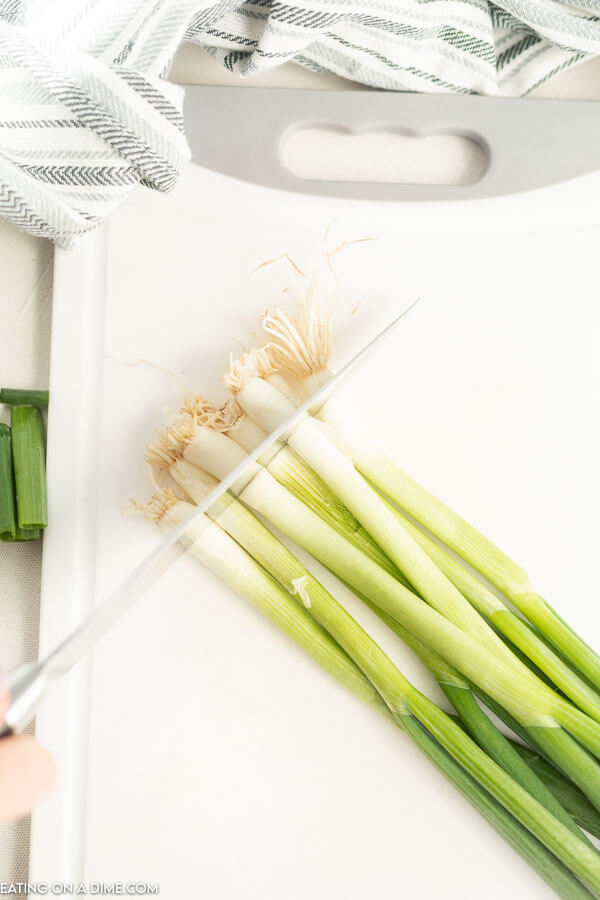 Close up image of the white part being cut on the cutting bard of a green onion. 