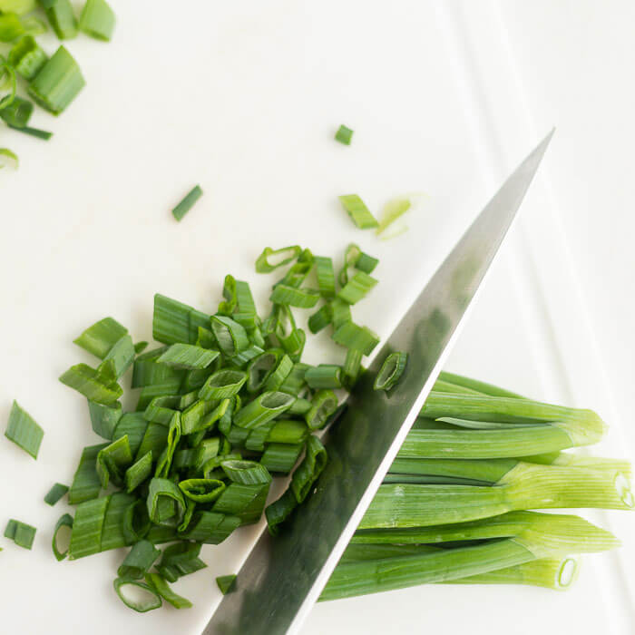 Close up image of chopped green onions on a cutting board with a knife. 