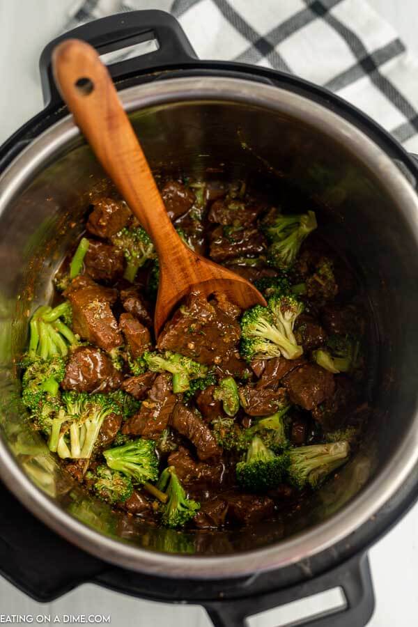 Close up image of beef and broccoli in the instant pot with a wooden spoon
