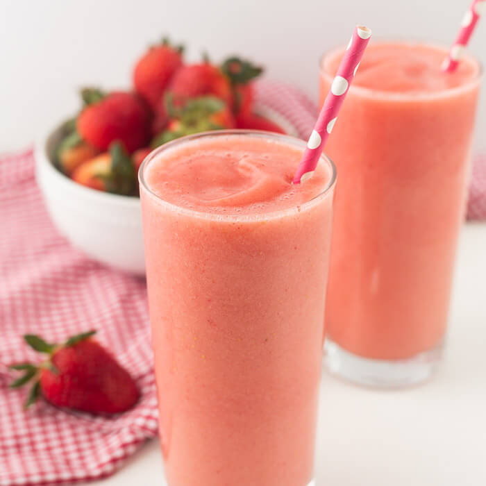 Close you caribbean way smoothie in a glass with a straw and a bowl of fresh strawberries. 