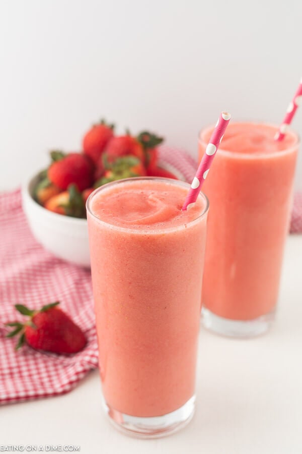 Close you caribbean way smoothie in a glass with a straw and a bowl of fresh strawberries. 