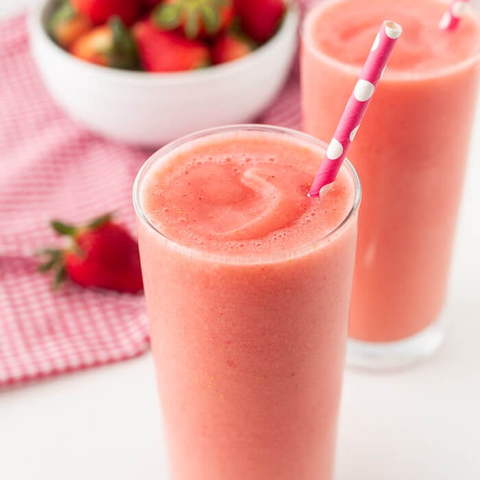 Close you caribbean way smoothie in a glass with a straw and a bowl of fresh strawberries. 