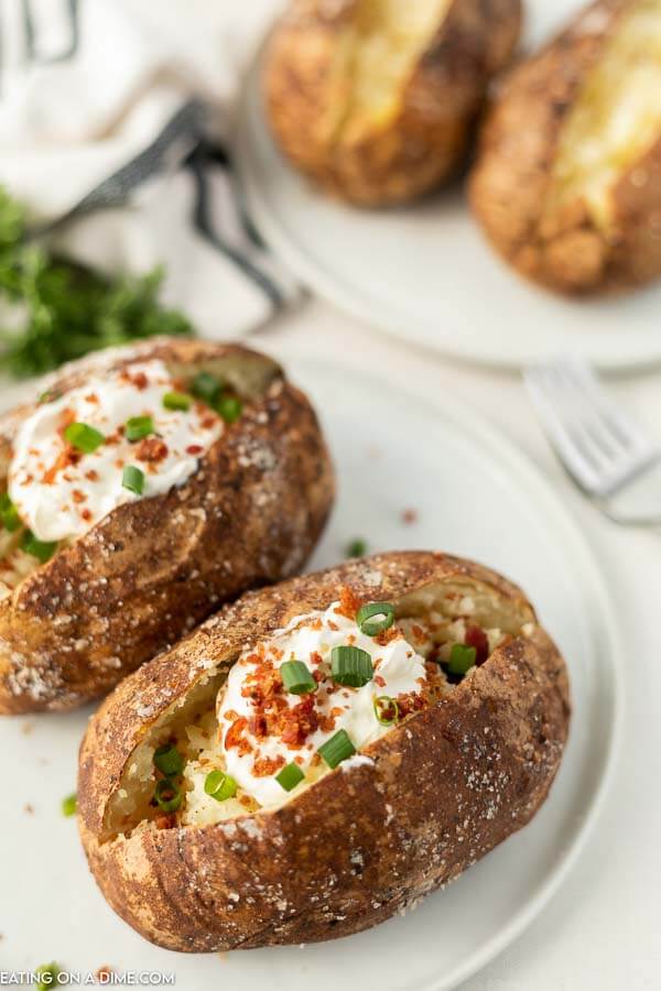 Close up image of two bake potatoes that on a plate and topped with sour cream, bacon bits and chives