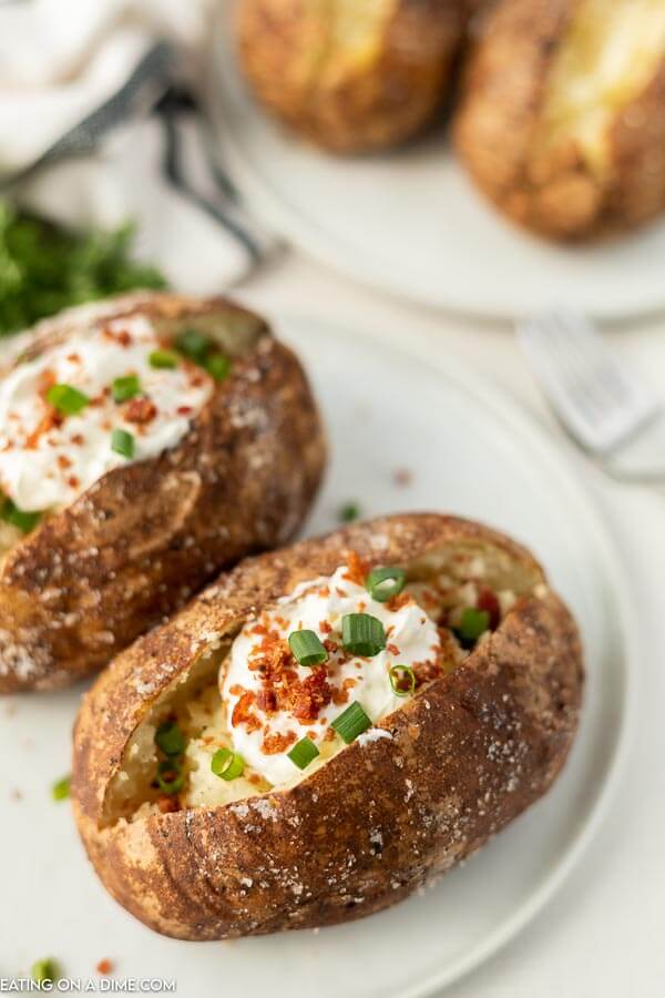 Close up image of two bake potatoes that on a plate and topped with sour cream, bacon bits and chives