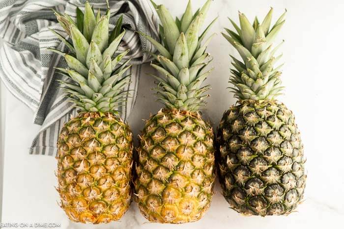 Close up image of three pineapples in different stages of ripening. 